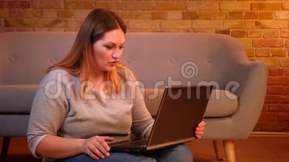 此外尺寸模型坐在地板上在笔记本电脑上的视频聊天在舒适的家庭氛围中体贴视频的预览图