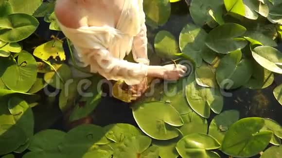 年轻的女人站在湖中在黄色的水的叶子里视频的预览图