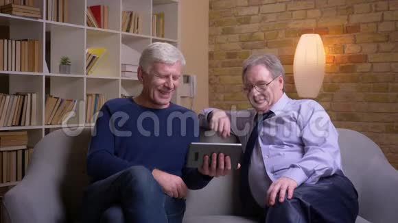 一幅老年男性朋友坐在沙发上在平板电脑上用视频聊天的肖像视频的预览图