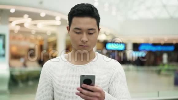 亚洲男性在模糊背景下用手机行走的慢动作中镜头视频的预览图