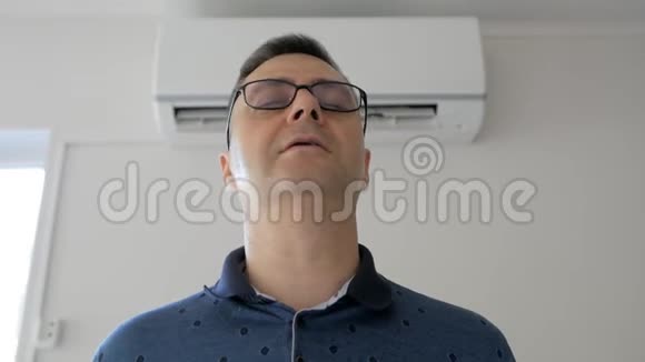 一个汗流浃背的人站在一台工作空调旁边的一股冷空气下冷却视频的预览图