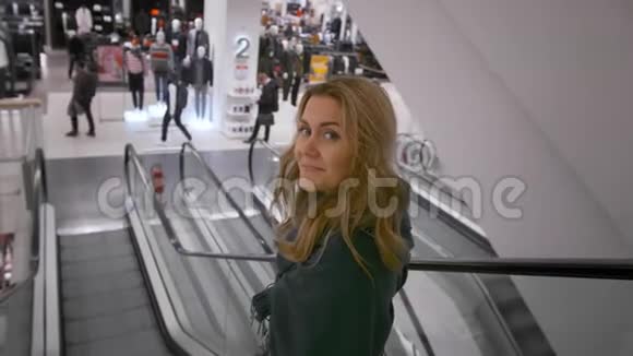 美丽的白种人女孩微笑着走下商场的自动扶梯在未获承认的买家的背景下视频的预览图
