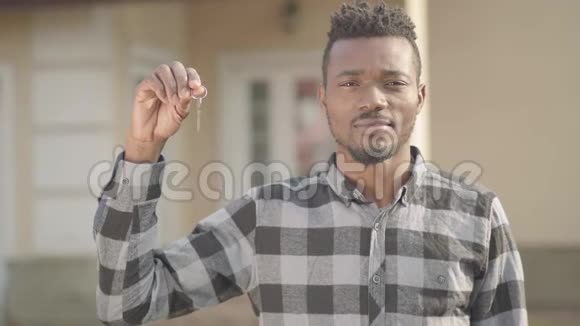 肖像自信英俊的非裔美国人穿着格子衬衫站在一所大房子前手里拿着钥匙视频的预览图