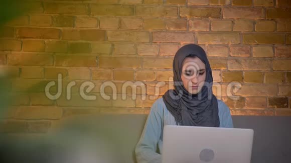 穆斯林年轻女商人戴头巾手持笔记本电脑坐着工作遥控器的特写侧景拍摄视频的预览图