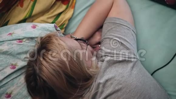 戴眼镜的女孩躺在沙发上在屏幕上看起来是一台笔记本电脑上面的景色视频的预览图