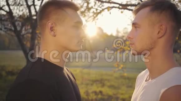 两个白人男孩在阳光下互相看着秋季公园里站在户外的成年运动员视频的预览图