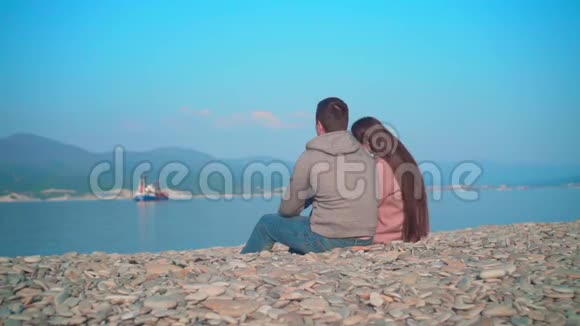 年轻女孩和一个男人坐在海滩上女孩把头靠在那家伙肩膀上视频的预览图