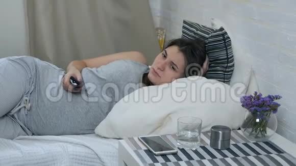 困倦的怀孕女孩躺在沙发上看电视打哈欠孕妇用遥控电视开关视频的预览图
