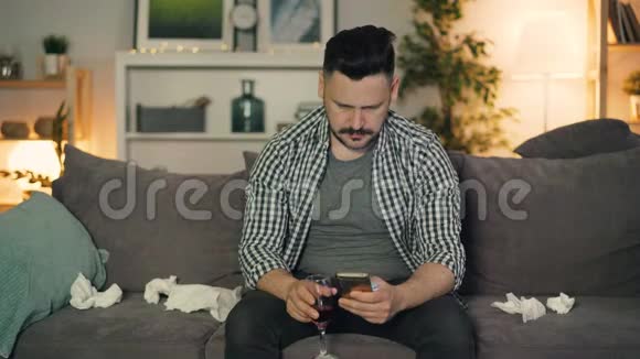 敏感的家伙哭着拿着一杯酒用智能手机坐在家里视频的预览图