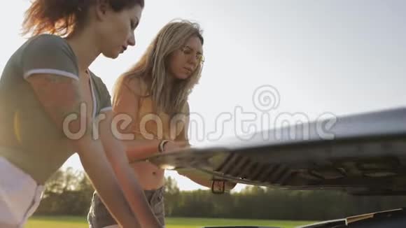 两个穿短裤的性感女孩和一件t恤在阳光下站在树林里的路上的敞篷汽车田野a视频的预览图