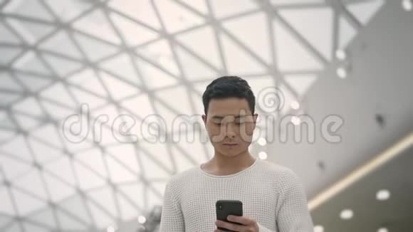 带着手机在天花板背景下行走的亚洲男性慢镜头视频的预览图