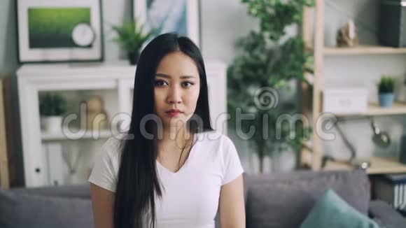 穿着白色T恤的迷人亚洲女孩的慢镜头肖像站在现代的房子里微笑着看着相机视频的预览图