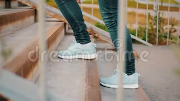 女腿穿着运动鞋和蓝色牛仔裤走在楼上室外女人的脚在运动鞋上爬楼梯视频的预览图