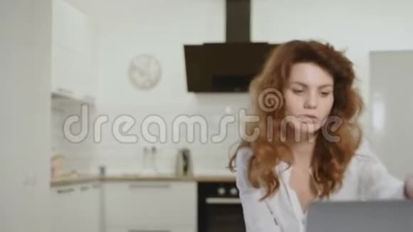 严肃的女人在开放式厨房接电话年轻女士在家里关闭笔记本电脑视频的预览图