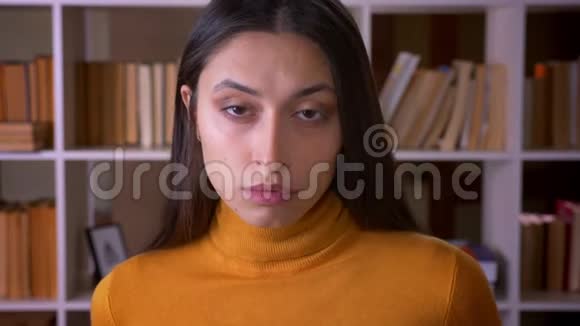 时尚的黑发女教师在书架背景上全神贯注地观看镜头的肖像视频的预览图