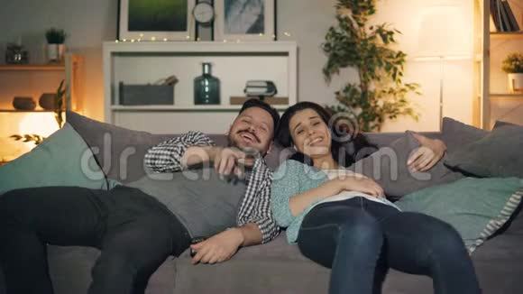 快乐的一对夫妇在晚上看电视笑着在家玩着聊天视频的预览图