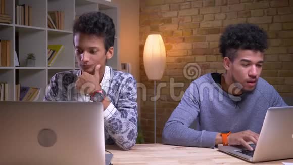 印度和非裔美国男学生使用笔记本电脑和在线学习的特写镜头一个问另一个视频的预览图