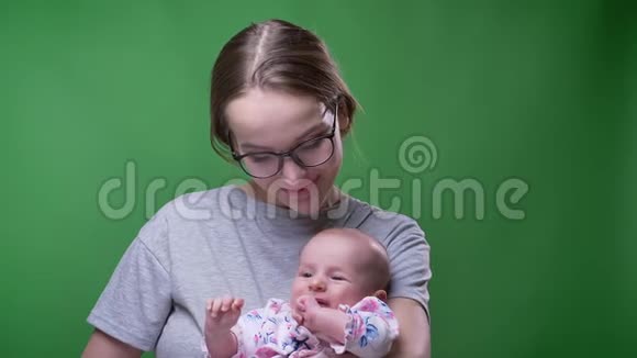 在绿色背景下美丽的母亲亲吻她可爱的哭泣的新生女儿的特写肖像视频的预览图