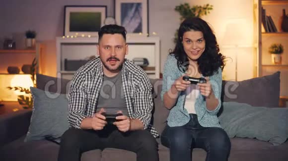 快乐的情侣女孩和男孩深夜在家玩电子游戏视频的预览图
