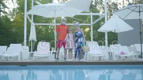 肖像快乐成熟的夫妇站在游泳池拥抱他们的小孙女祖母和祖母视频的预览图