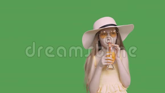 年轻的少女戴着黄色眼镜戴着帽子在绿色屏幕上喝鸡尾酒视频的预览图