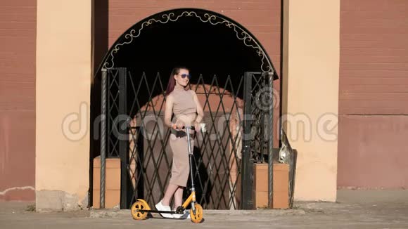 年轻漂亮的女人穿着裙子和太阳镜在砖墙的背景上骑着一辆踢踏板车兵马俑视频的预览图