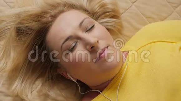 闭上美丽的女人躺在床上听音乐视频的预览图