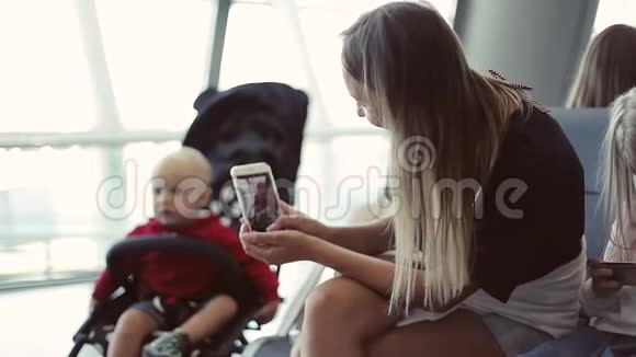 一位年轻的母亲用手机在婴儿车里给她的小儿子拍照视频的预览图