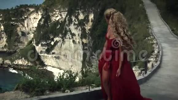 年轻女子穿着优雅的红色长裙在悬崖上行走视频的预览图