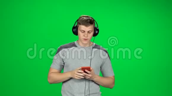 戴着大耳机的人在工作室的绿色屏幕上用智能手机发短信视频的预览图