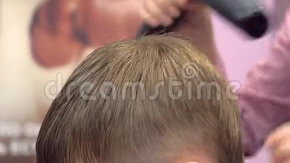 理发师在男孩的头上理发后用吹风机头发发型师双手特写侧视视频的预览图