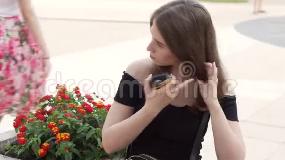 一个漂亮的女孩坐在城市街道的长椅上梳头视频的预览图