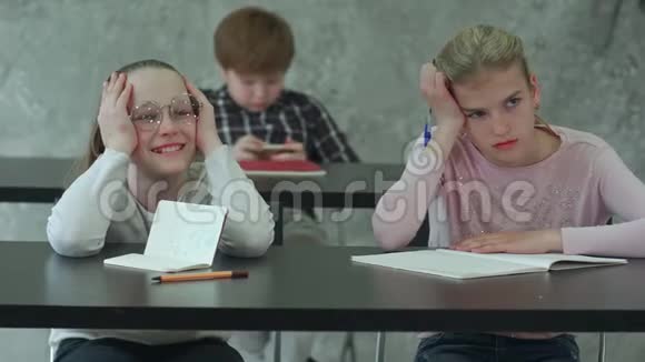 无聊的女孩坐在学校教室的桌子上和同学讨论一些事情视频的预览图