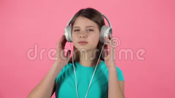小雌性在粉色背景上用白色大耳机听音乐和跳舞慢动作视频的预览图