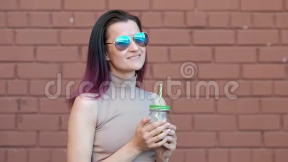戴着墨镜的年轻美女正在喝着杯中的柠檬水鸡尾酒背景是一根吸管视频的预览图