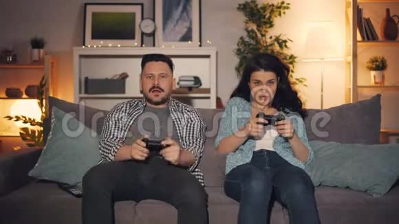 夫妻俩在家里坐在沙发上玩电子游戏手里拿着操纵杆视频的预览图