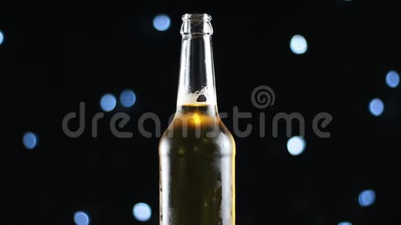 一瓶开着的金色啤酒在黑色背景上旋转灯光明亮视频的预览图