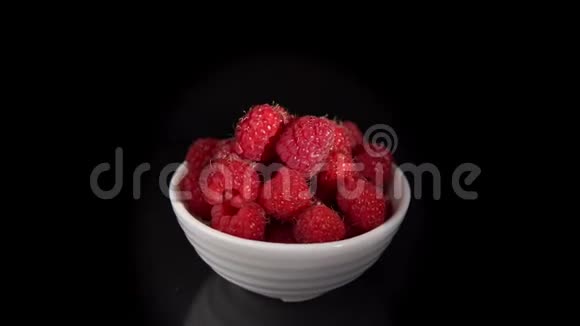 一堆红色成熟的覆盆子放在白色的小杯子里围绕着黑色的背景视频的预览图