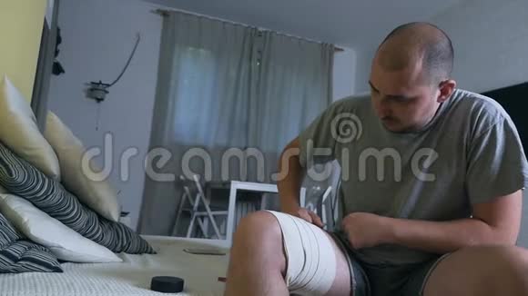 一个年轻的秃头用药膏涂抹一条疼痛的腿和瘀伤紫罗兰腿运动性足部损伤视频的预览图