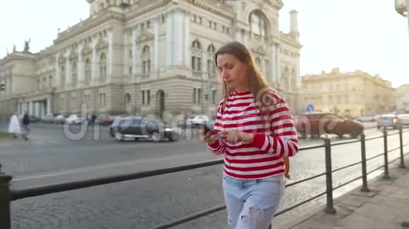 女人走在一条老街上日落时分在智能手机上聊天视频的预览图