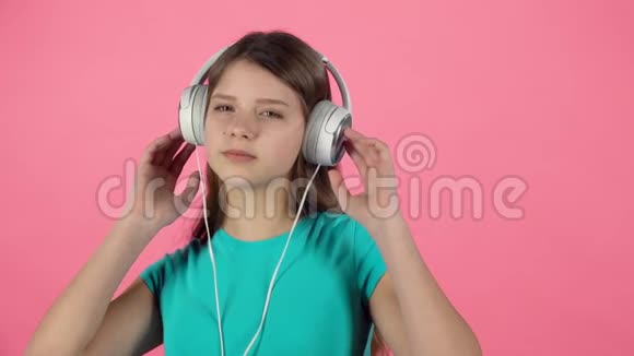 女孩听音乐和舞蹈在粉红色背景的白色大耳机慢动作视频的预览图