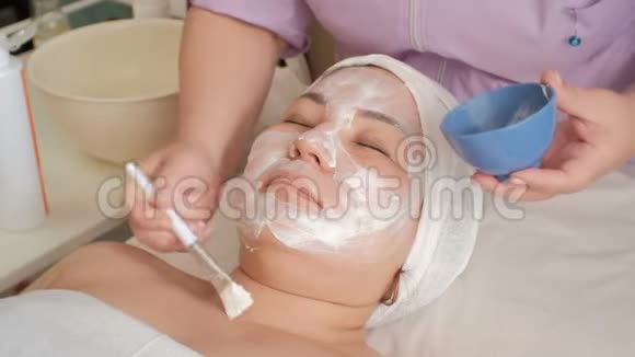 一个在美容院的亚洲女孩的脸美容师给一个带br的穆斯林女人的颈部涂上一层白色按摩霜视频的预览图