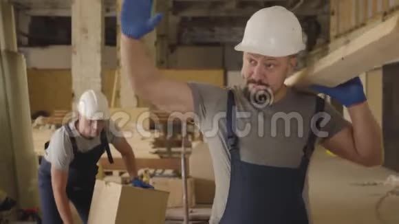 肌肉发达的白种人戴着白色防护头盔用木板在施工现场行走建设者停止视频的预览图