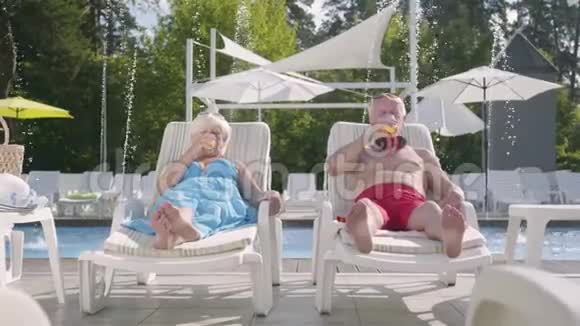 成熟的夫妇躺在游泳池附近的日光浴床上喝着果汁交谈着微笑着充满爱意的家庭康乐及文化事务署视频的预览图