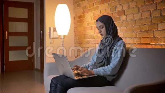 年轻迷人的穆斯林少女戴着头巾坐着时使用笔记本电脑和视频通话的特写镜头视频的预览图