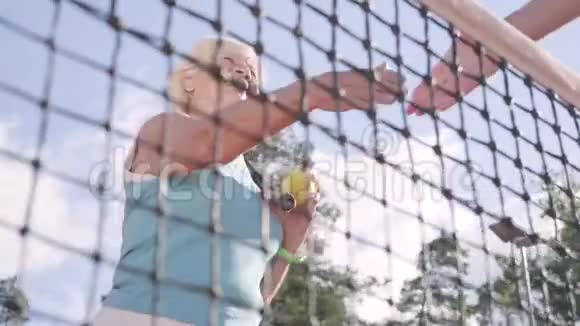成年女子与一个未被认出的对手握手站在夏日阳光下的网球场上娱乐视频的预览图