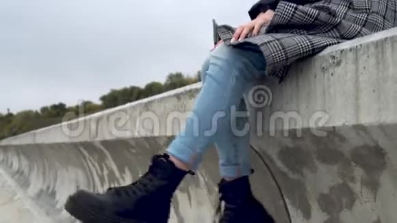 年轻女子坐在风中的水泥栅栏上摇着腿视频的预览图