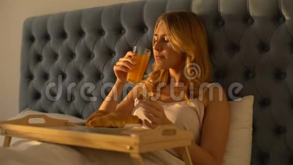 女人在床上喝橙汁吃美味的牛角面包健康的早餐视频的预览图