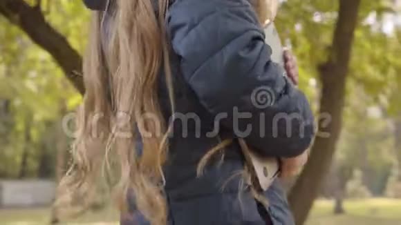 一只十几岁的白人女性手拿着笔记本电脑秋天年轻的女学生带着她的装置走路视频的预览图