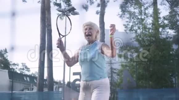 快乐成熟的女人赢得了网球锦标赛这位老太太在赢球时用球拍举起双手视频的预览图